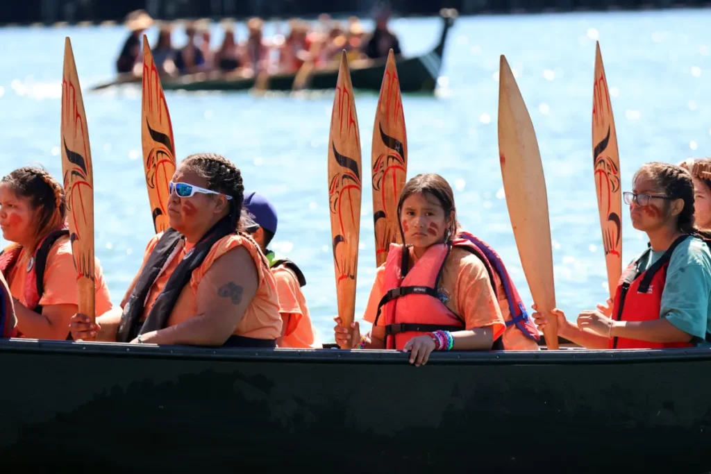 Aaliyah James,11, Pacheedaht, raises her paddle while sitting in the canoe Sea Foam Dancer